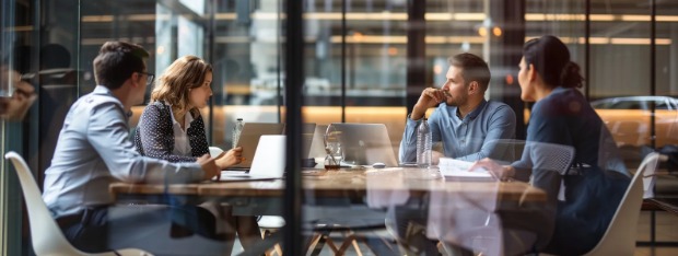 Four professionals having a business meeting at a large desk and discussing account planning systems